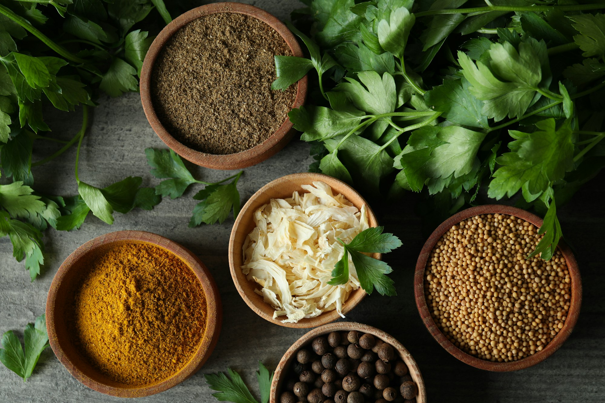 Different spices in wooden bowls on gray textured background